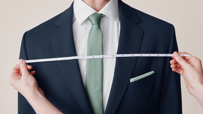 Man in navy suit being measured with a measuring tape held across his chest.