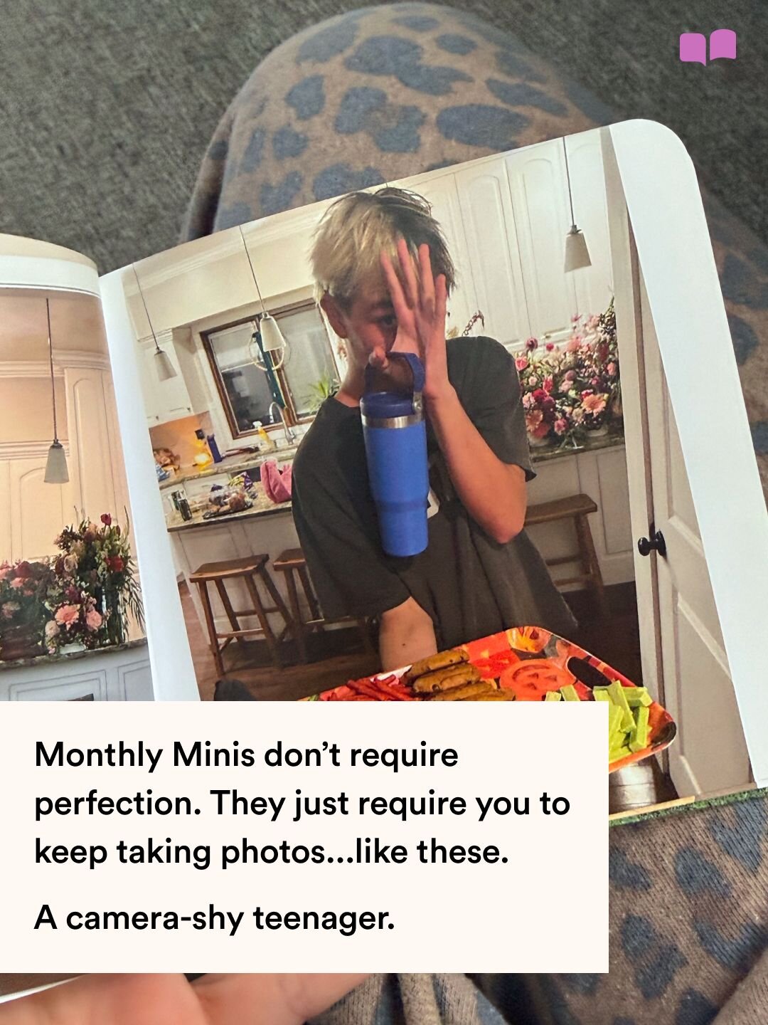 A Monthly Mini photo book open to a page showing a teenager covering his face in a kitchen, with text about imperfect everyday photos