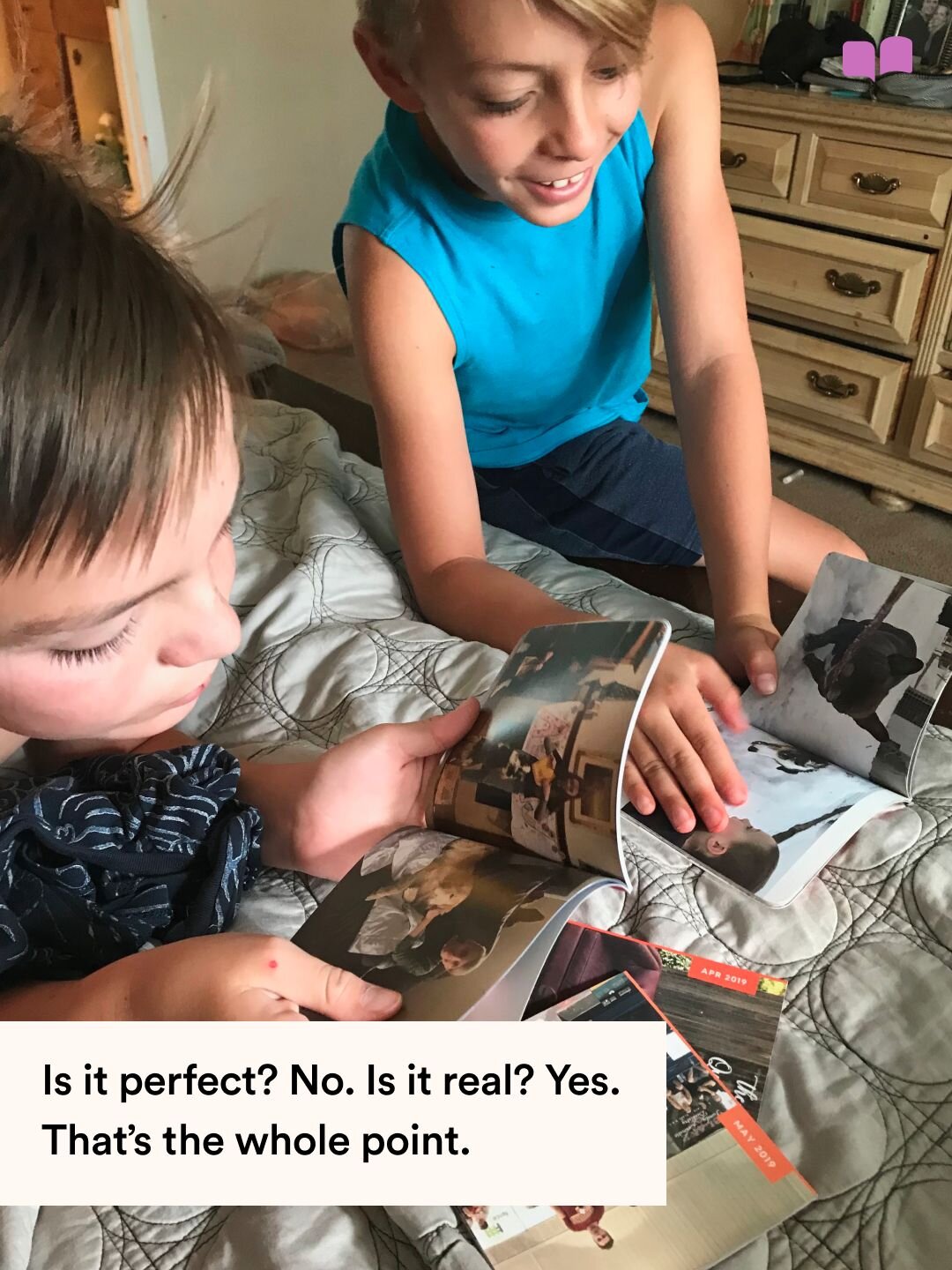 Two boys sitting on a bed looking through a Monthly Mini photo book together, with text reading Is it perfect? No. Is it real? Yes. That is the whole point.