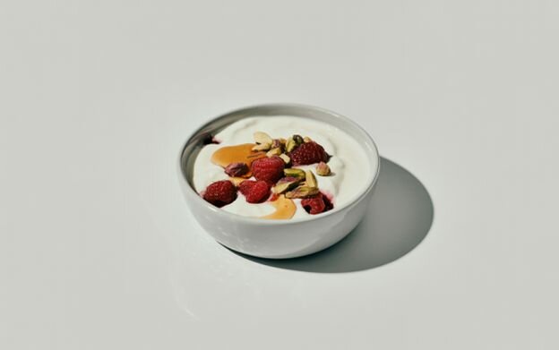 Plain Greek yogurt topped with raspberries, pistachios, and honey, a creamy, high-protein snack under 100 calories for balanced nutrition