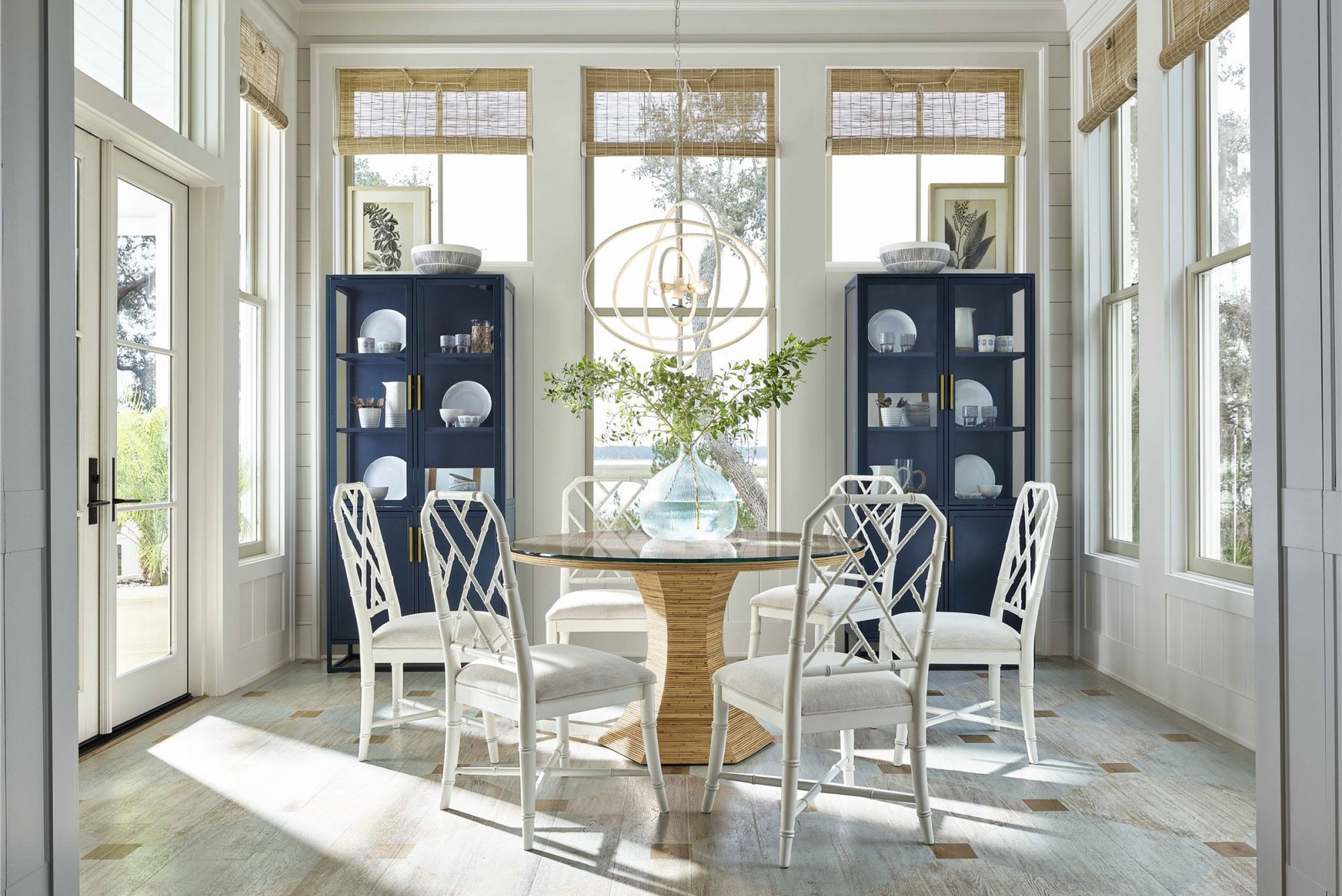 Bright dining room featuring a round rattan table with a glass top and white bamboo chairs. Two matching blue cabinets add a touch of color.