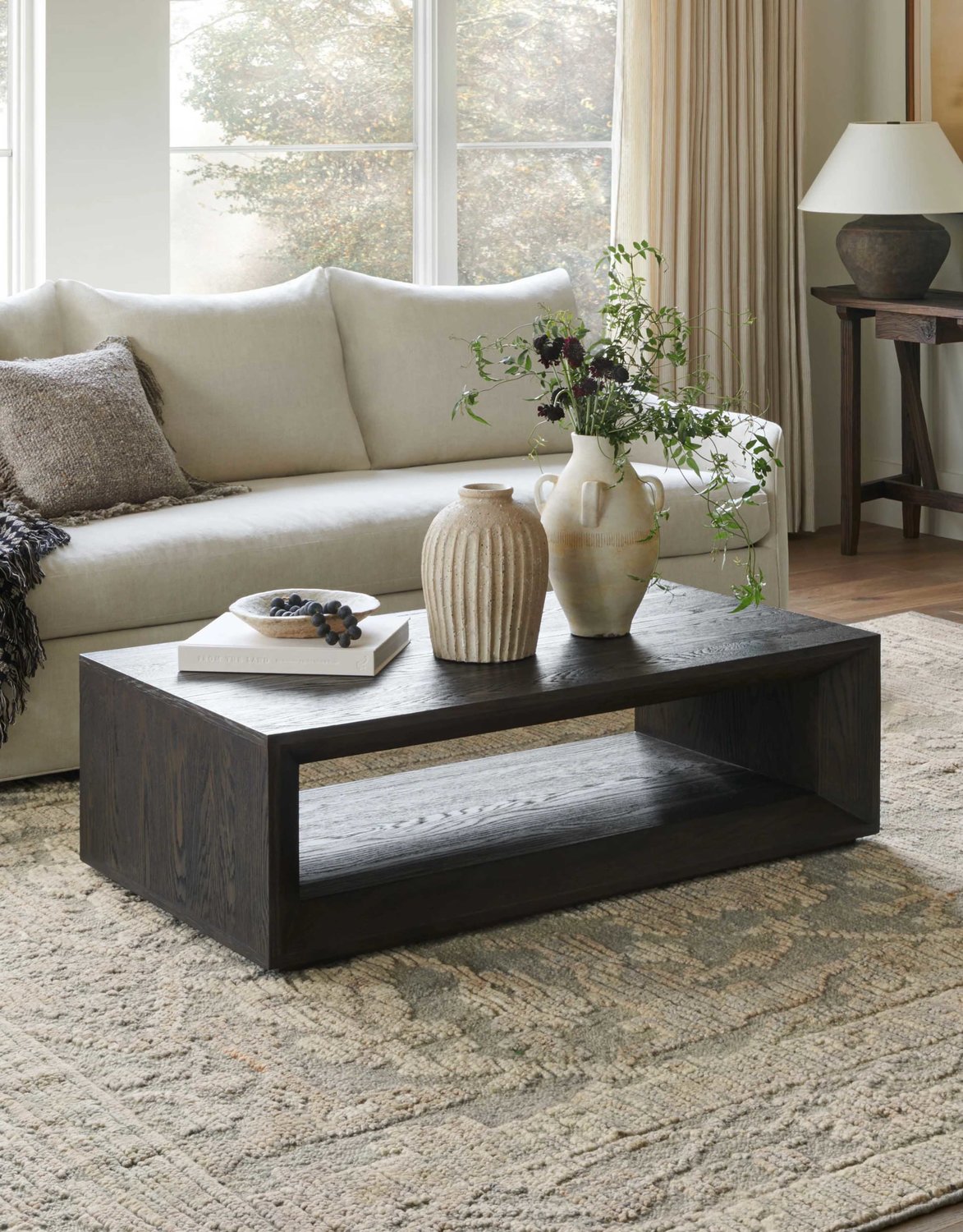 Black wooden coffee table in front of white sofa on top of neutral rug