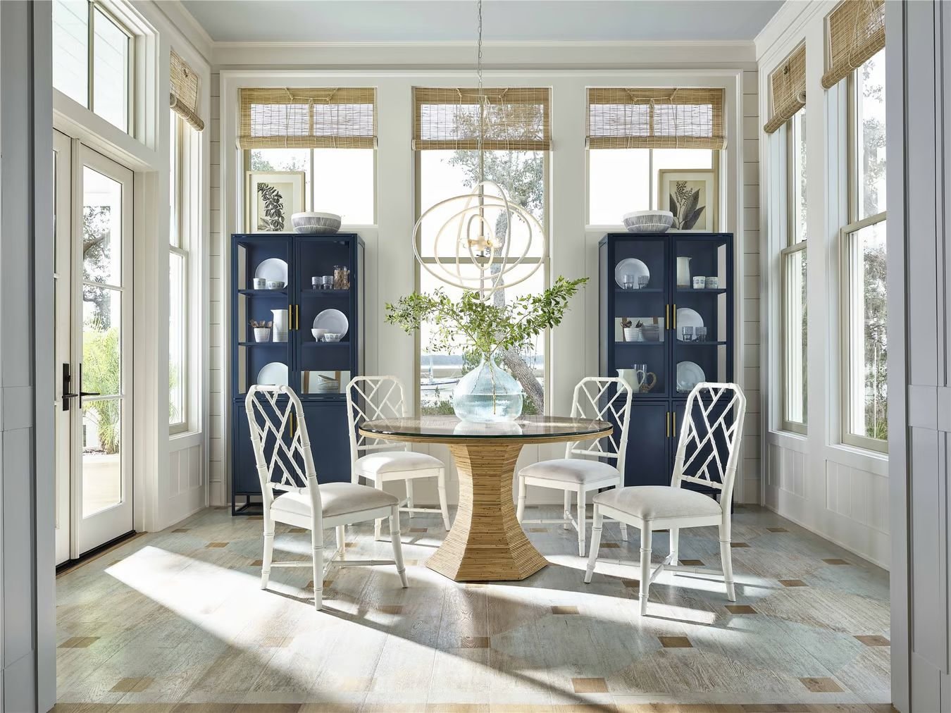 Bright dining room featuring a round rattan table with a glass top and white bamboo chairs. Two matching blue cabinets add a touch of color.