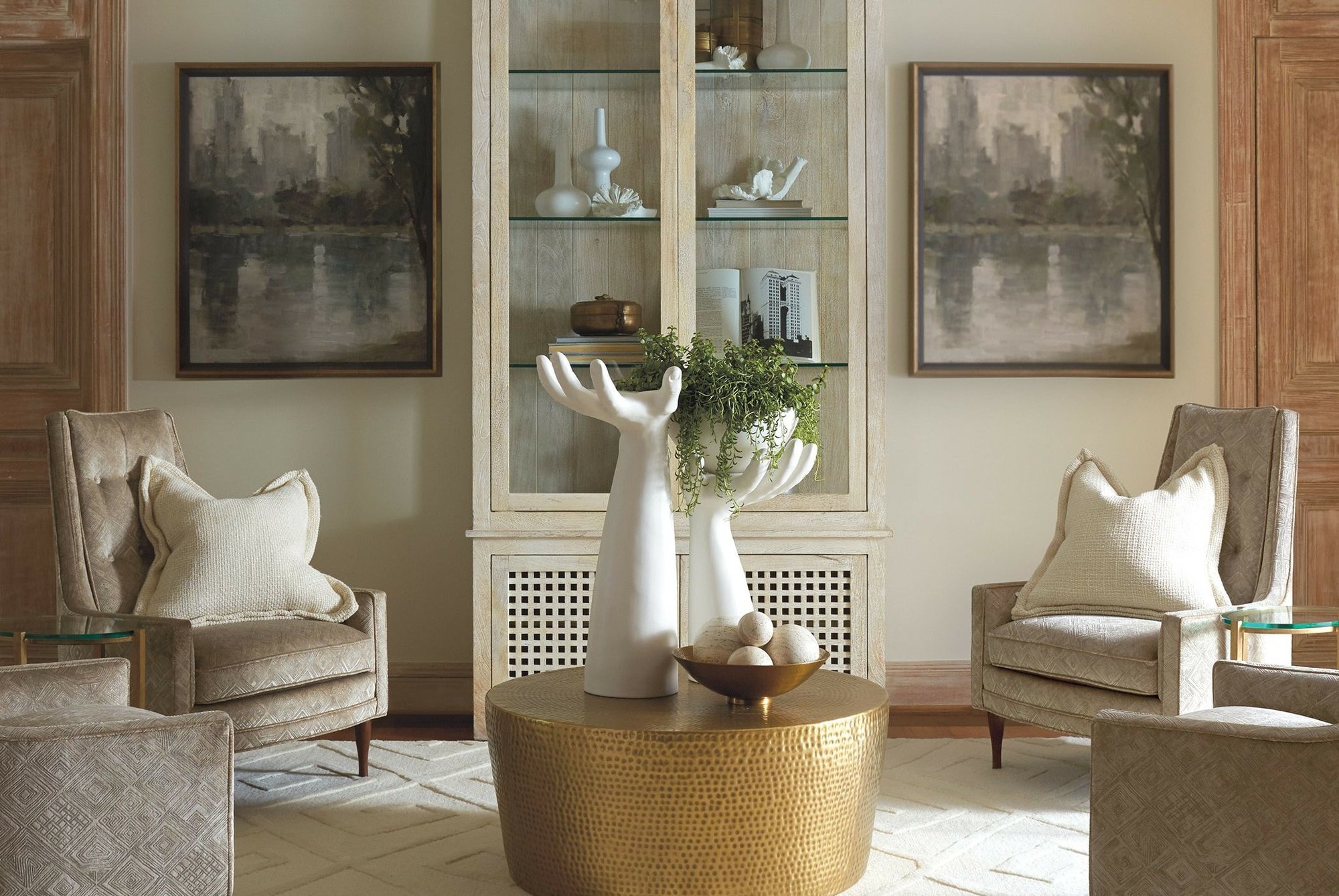 Sitting area with two large hand-shaped candle holders ontop of a gold hammered coffee table, surrounded by four matching beige upholstered chairs.