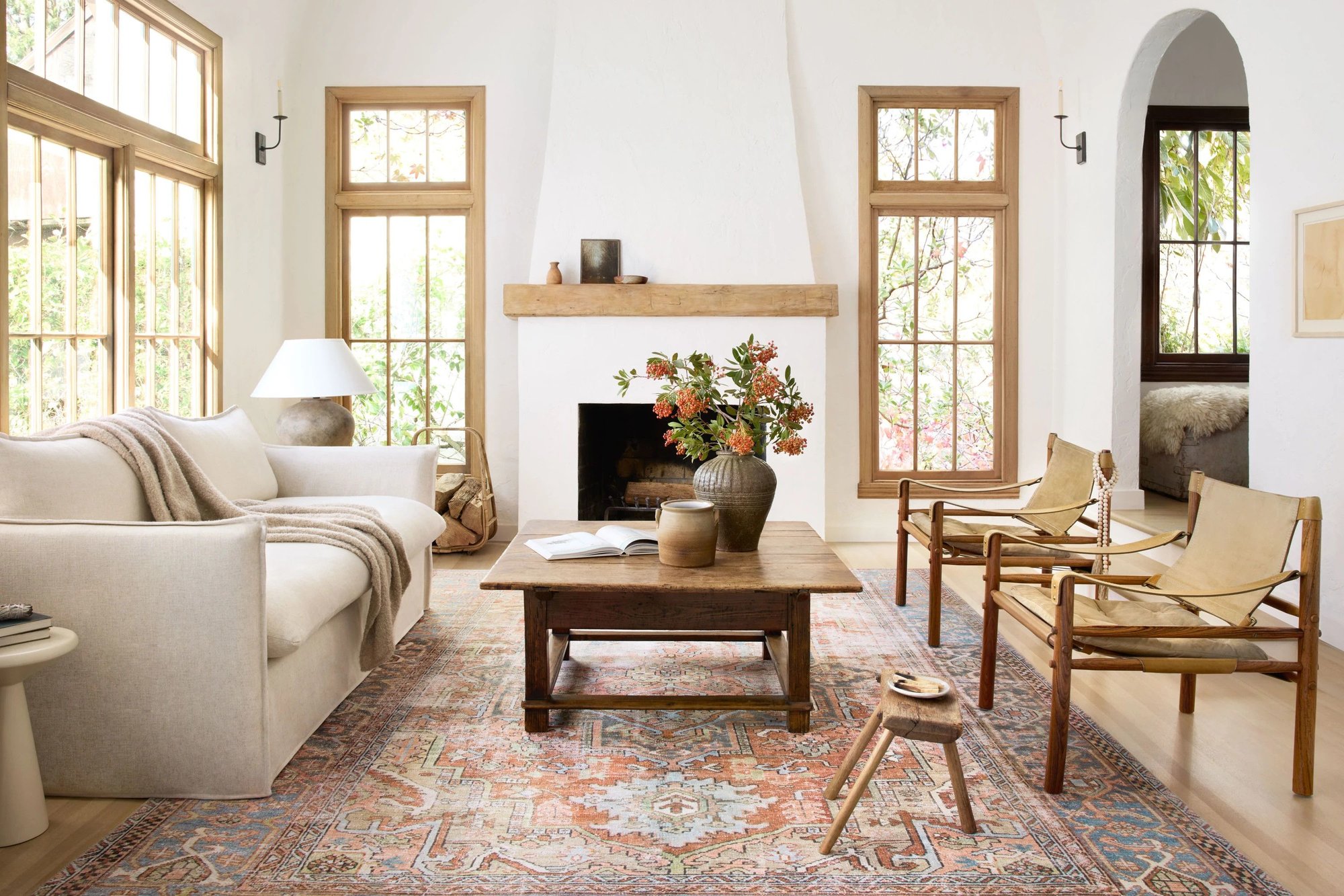 Modern farmhouse style dining room featuring a round wooden table surrounded by four black dining chairs. A neutral rug anchors the space, and ceramic vases adorn the table, blending rustic charm with contemporary design.