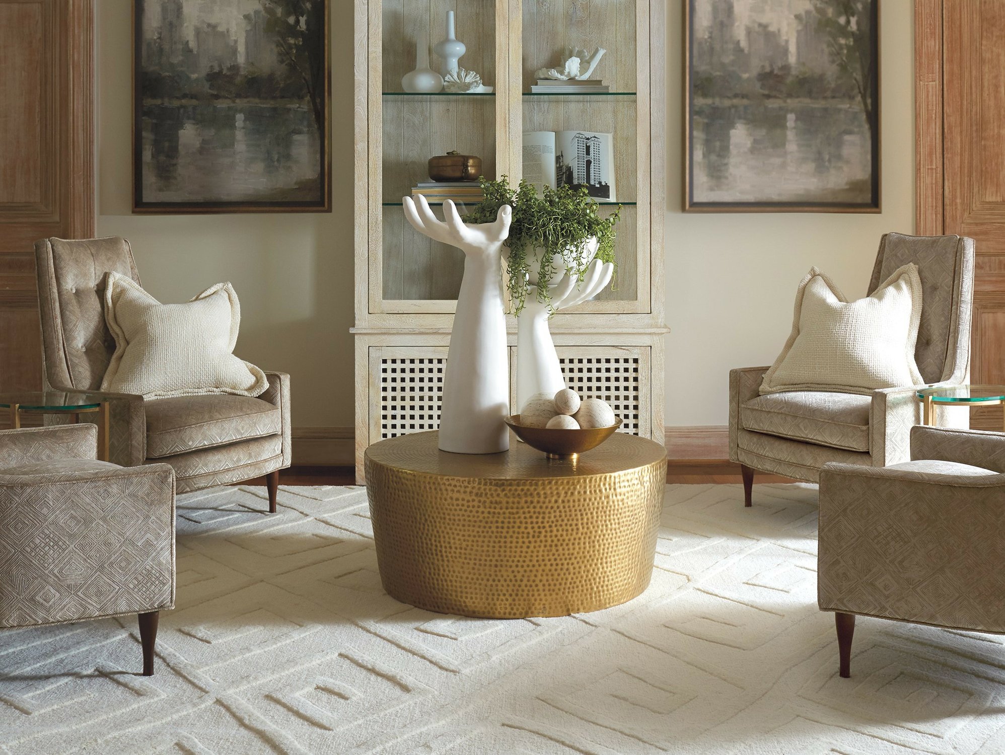Sitting area with two large hand-shaped candle holders ontop of a gold hammered coffee table, surrounded by four matching beige upholstered chairs.