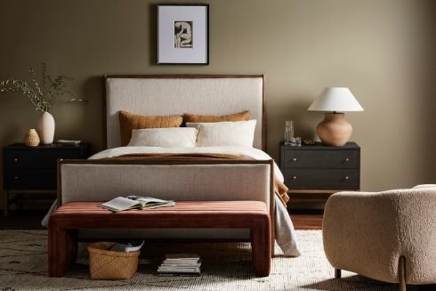 Bedroom showcasing a soothing neutral color palette. An upholstered headboard is accompanied by two matching black nightstands. A brown bench rests at the foot of the bed and a beige rug ties the space together.