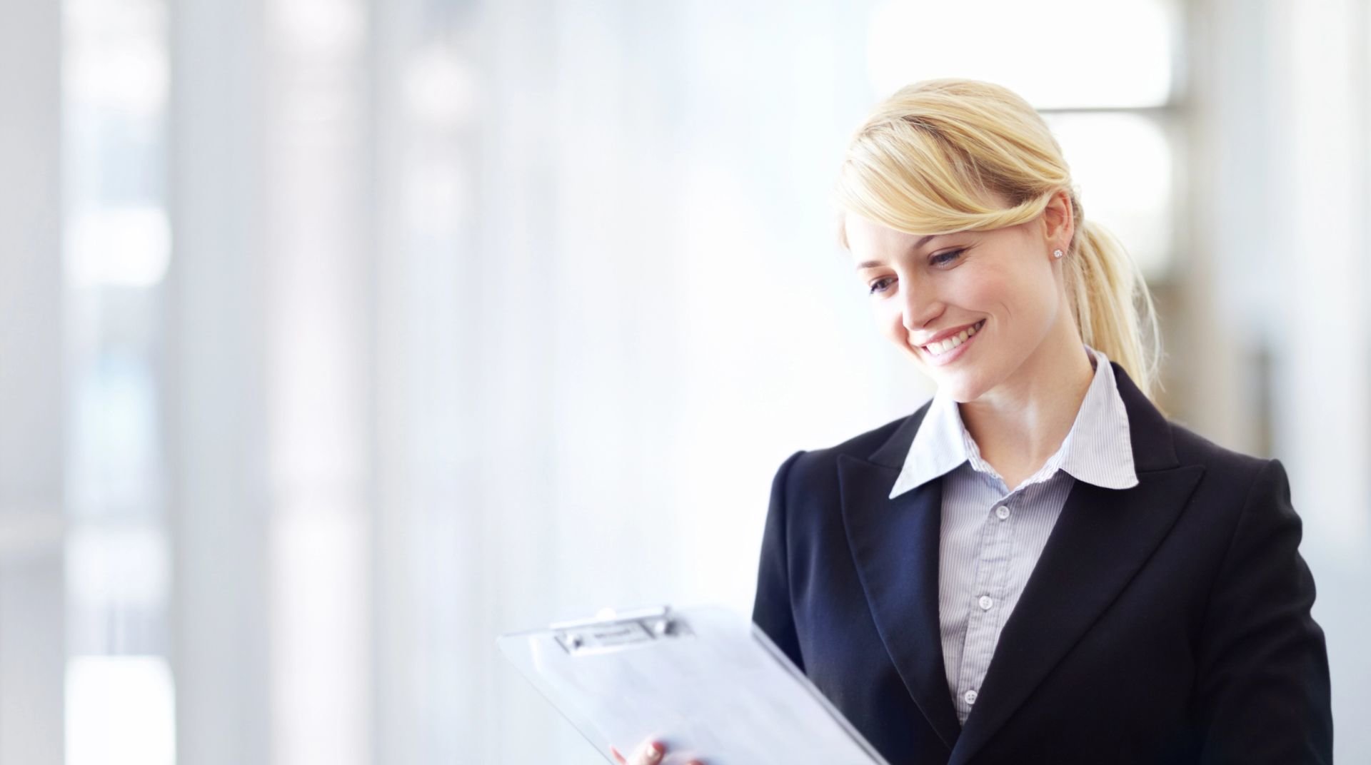 Color photo of blonde professional woman holding a clipboard.               