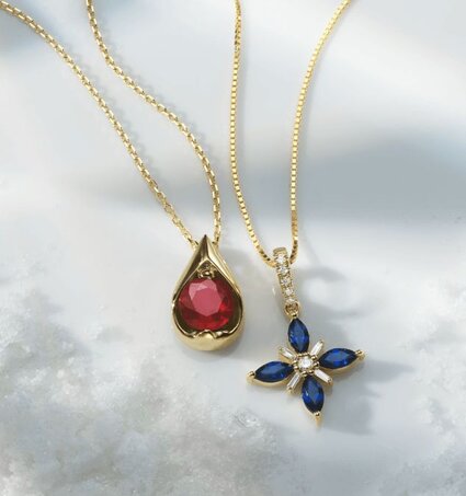 A solitaire gemstone pendant and a gemstone and diamond flower pendant surrounded by snow.