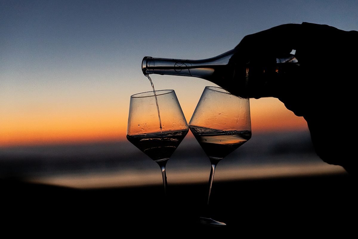 A bottle pouring wine into two glasses with the sunset in the background