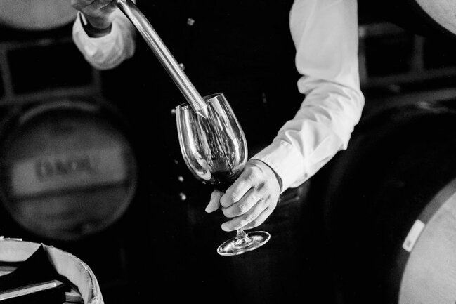 A winemaker tests wine out of a barrel