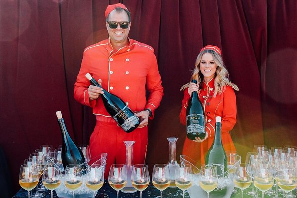 People in costume serve glasses of wine out of large bottles