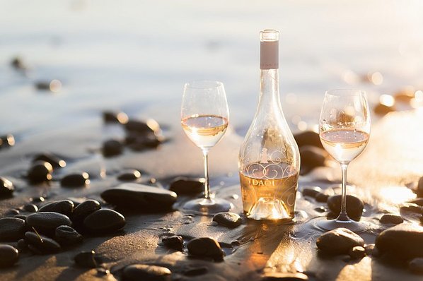 A bottle of rosé and two full wine glasses on the beach 