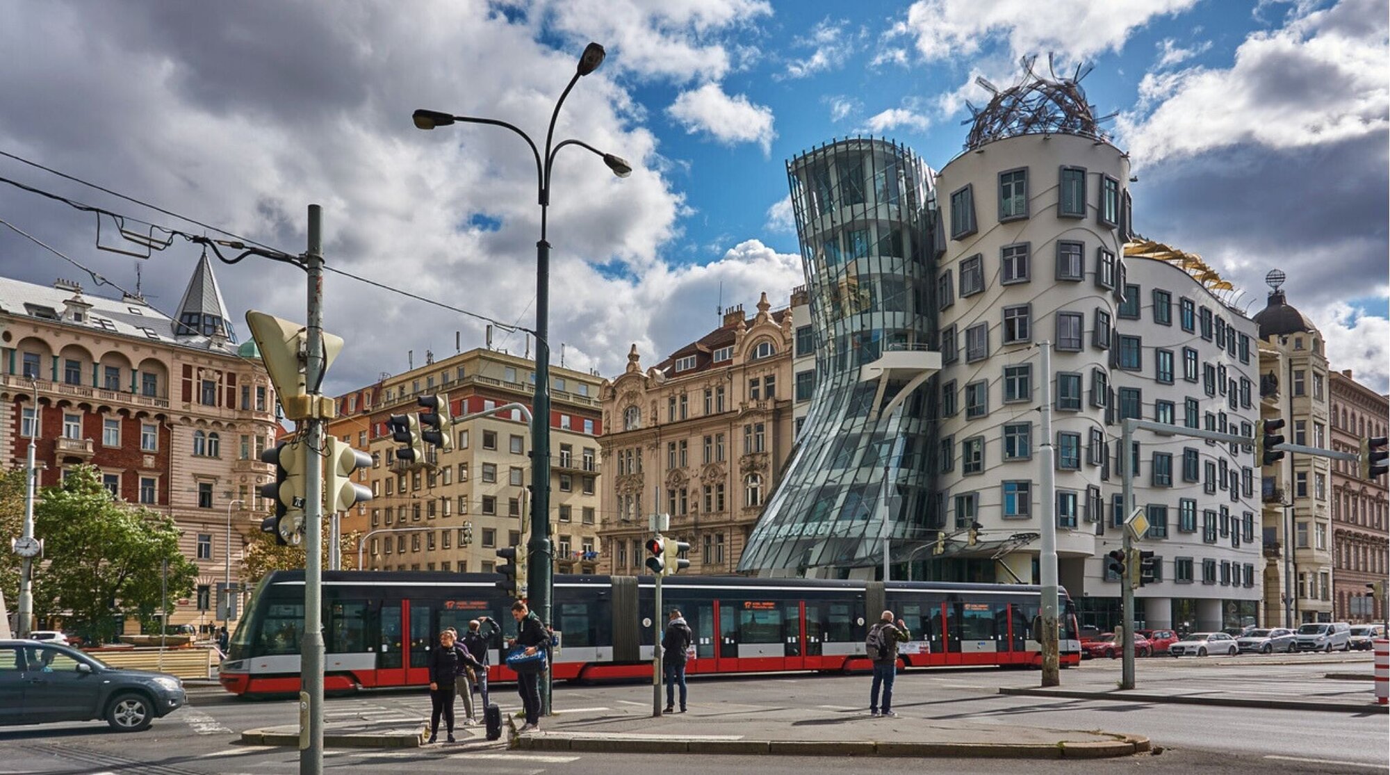 Pedestres, veículos e um bonde na rua Rašínovo Nábřeží. Ao fundo, o edifício Dancing House de Praga.