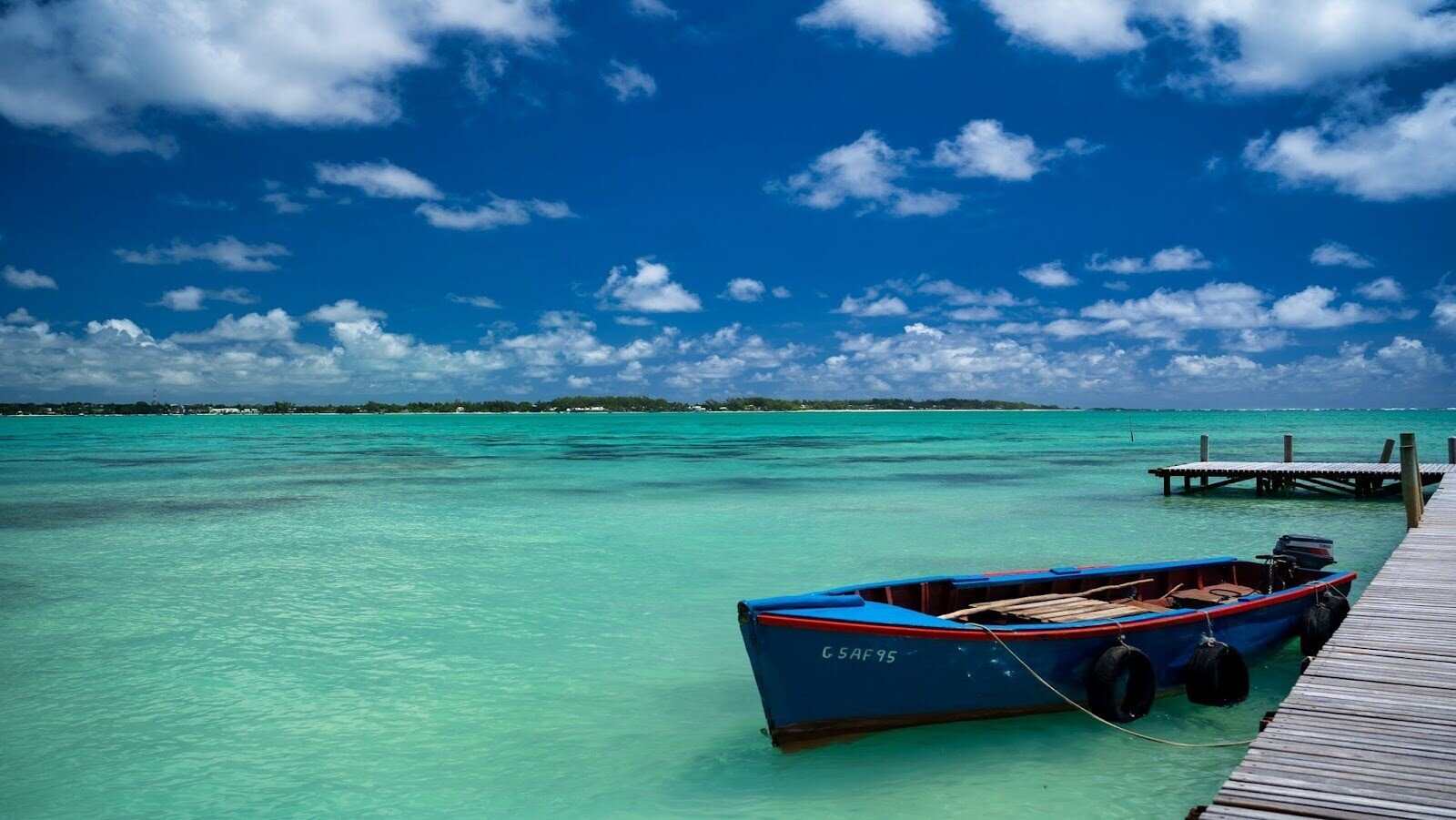 Red and blue boat achored to a deck on large body of water 