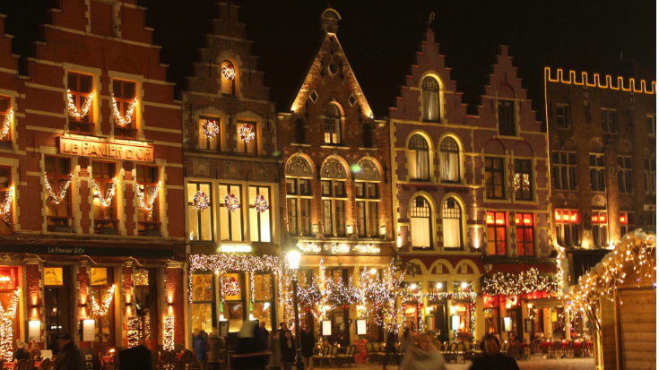 An image at night time of a row of traditional Belgian houses in Bruges, lit by soft yellow lights and decorated with Christmas fairy lights.To illustrate a blog post entitled 'Extreme Day Trips: Eurostar Christmas Markets Edition'.