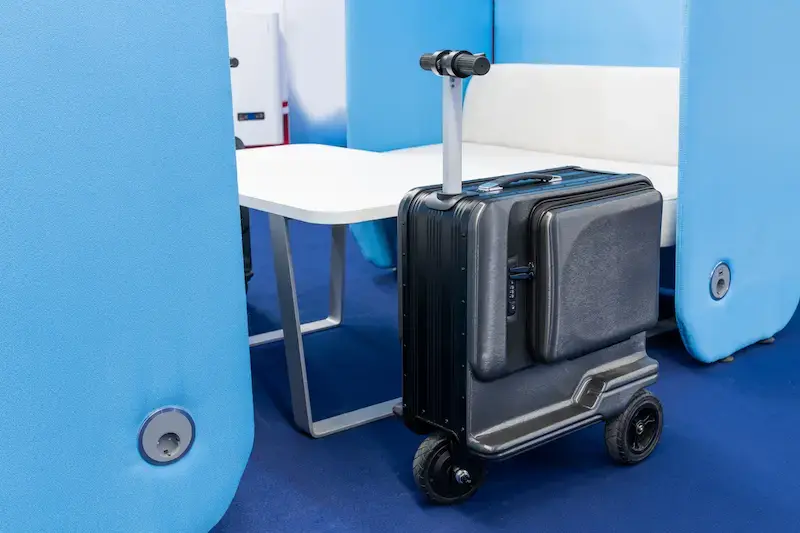 Valise connectée à roulettes avec poignée télescopique, stationnée dans un espace avec table et cloisons bleues