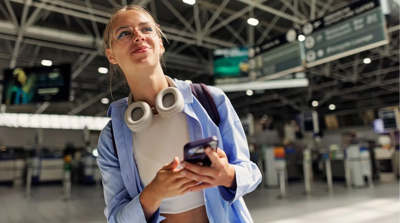 Foto de jovem turista no aeroporto com celular em mãos.