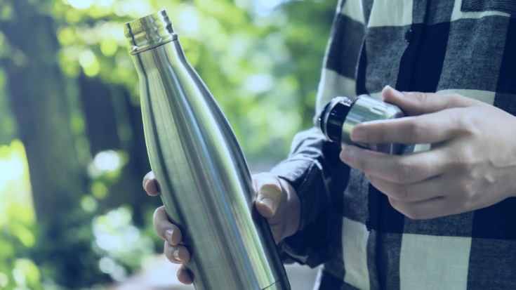An image of a man's hand holding an aluminium reusable water bottle, to illustrate the advice to take an empty water bottle into Summer Sonic Festival in Japan.