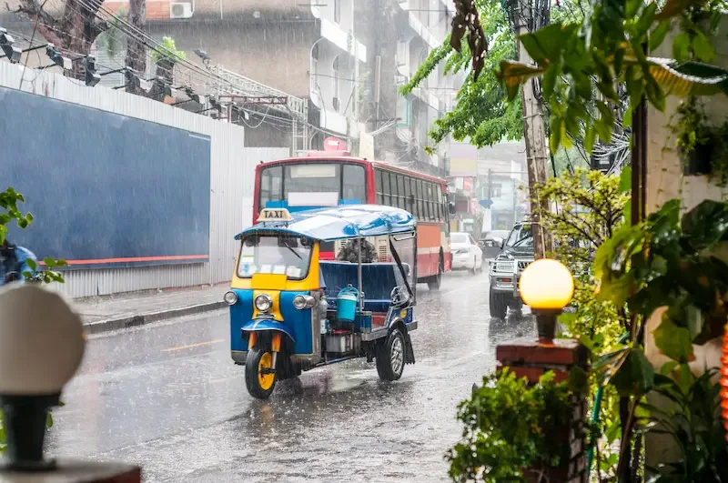 A tuk-tuk driving through heavy rain in Bangkok.
