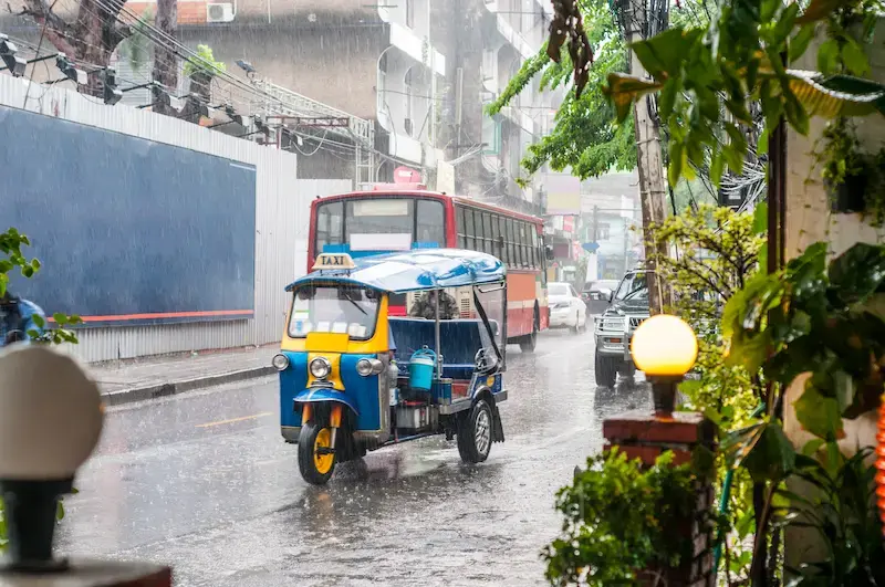 A tuk-tuk driving through heavy rain in Bangkok.