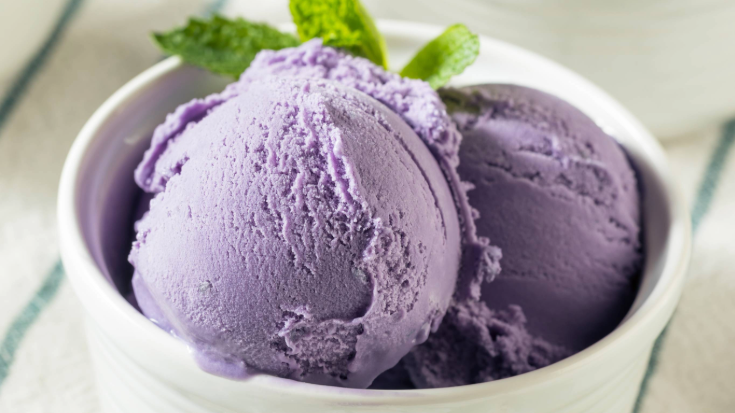 A colour photograph showing a close-up of a scoop or purple ice cream, which has a mint leaf placed in it. Beni-imo ice cream is made from the native purple sweet potatoes of Okinawa. To illustrate a blog post entitled 'Top Things to Do in Okinawa, Japan's Tropical Gem.'