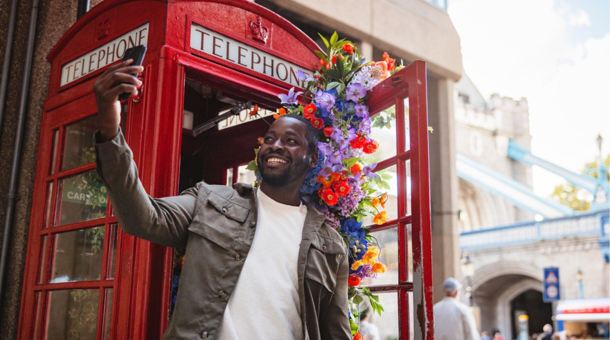 Turista sorridente tirando fotos perto da icônica cabine telefônica vermelha em Londres.