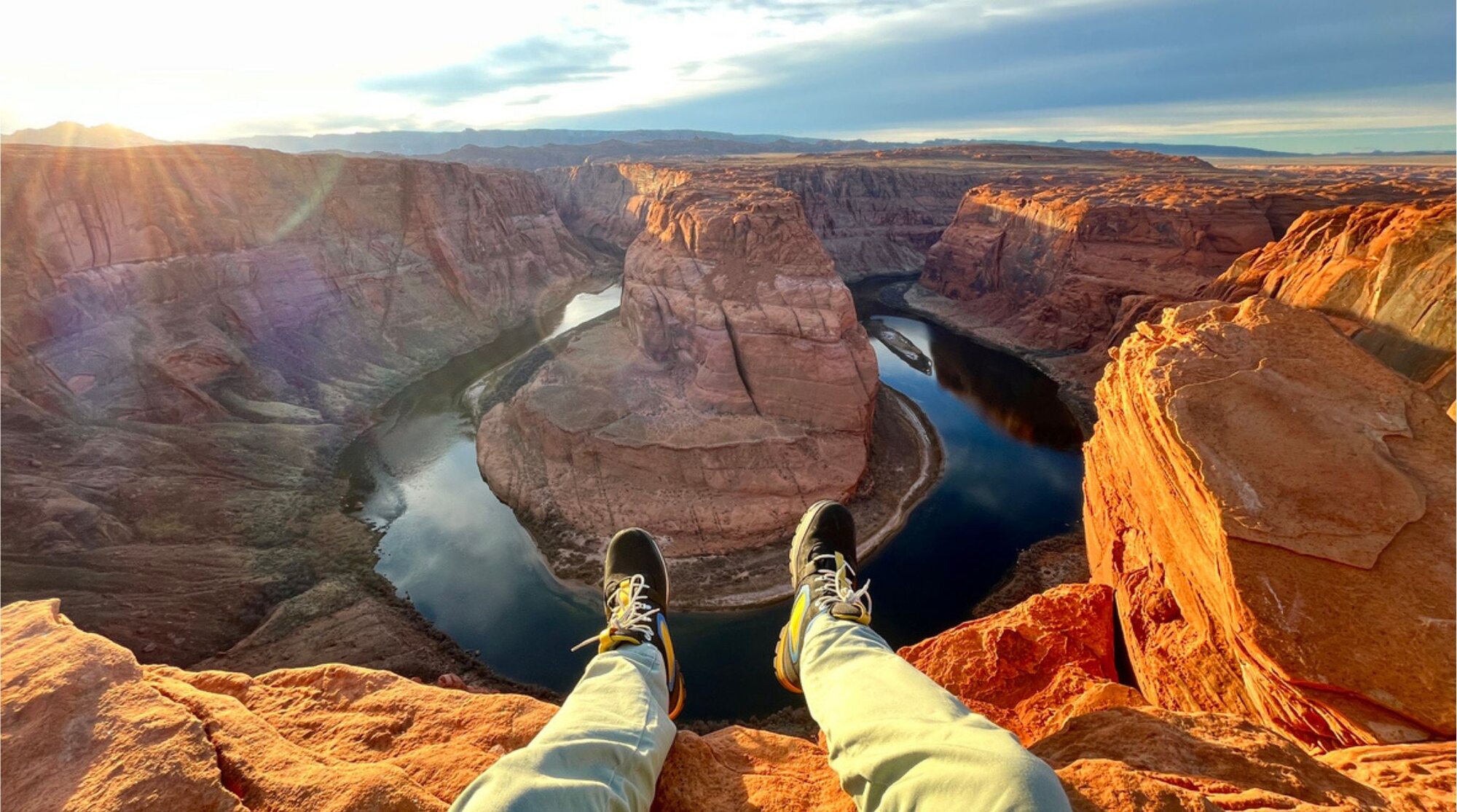 Una persona sentada en un acantilado mirando hacia un río en forma de herradura entre cañones de Grand Canyon, con luz de tarde.