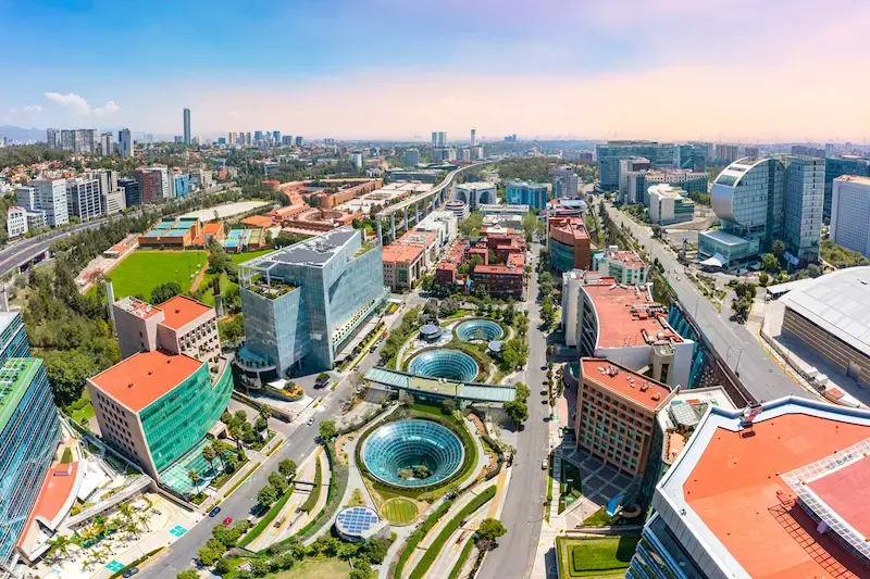 Vista aérea de Santa Fe en Ciudad de México con edificios modernos, avenidas y fuentes circulares.
