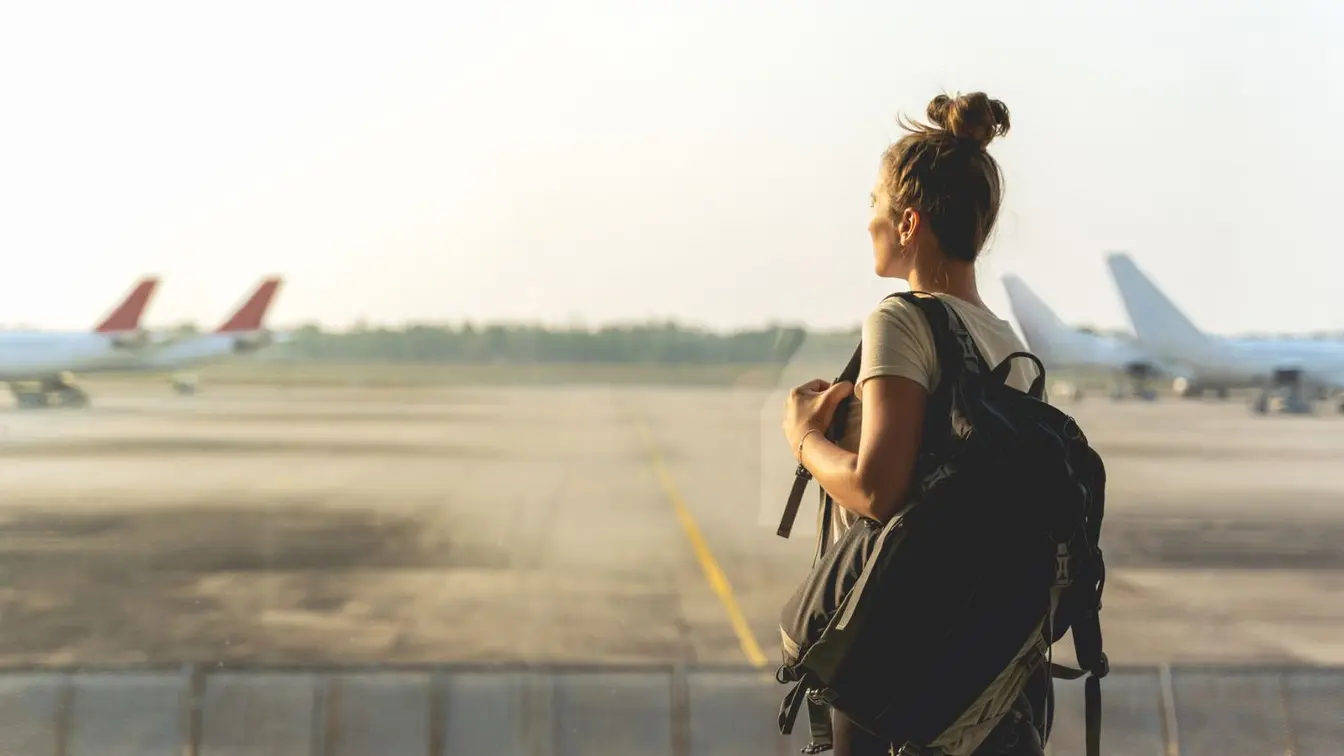 Eine Frau mit Kurztrip-Idee steht am Flughafen am Fenster