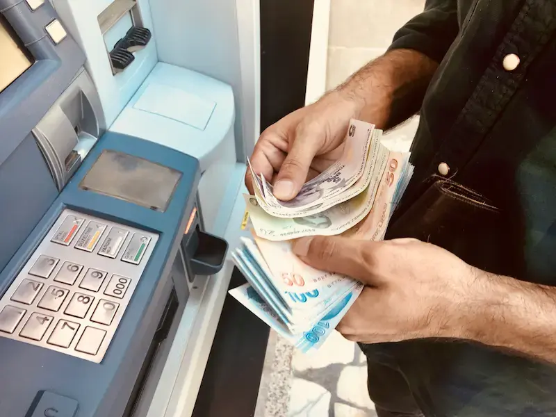 Voyageur retirant et comptant des billets de livre turque devant un distributeur automatique en Turquie.