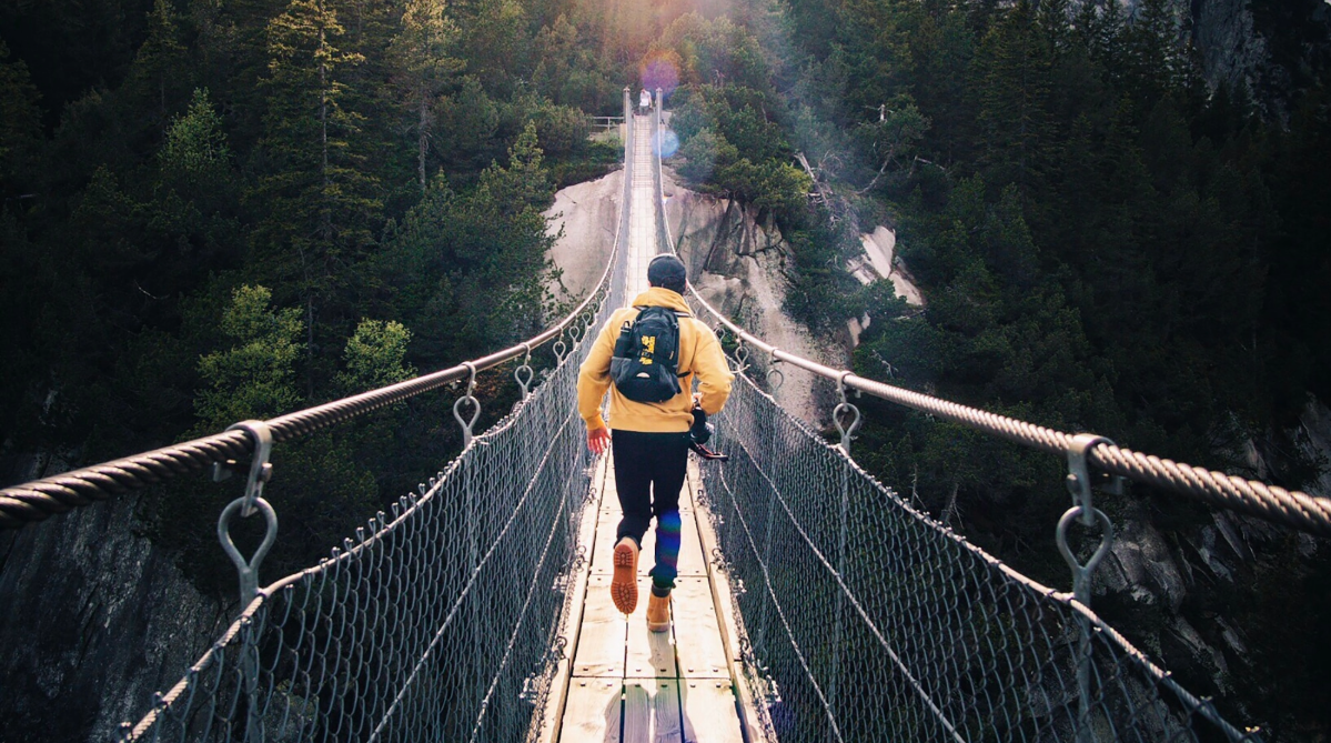 traveler running across a bridge wearing a backpack