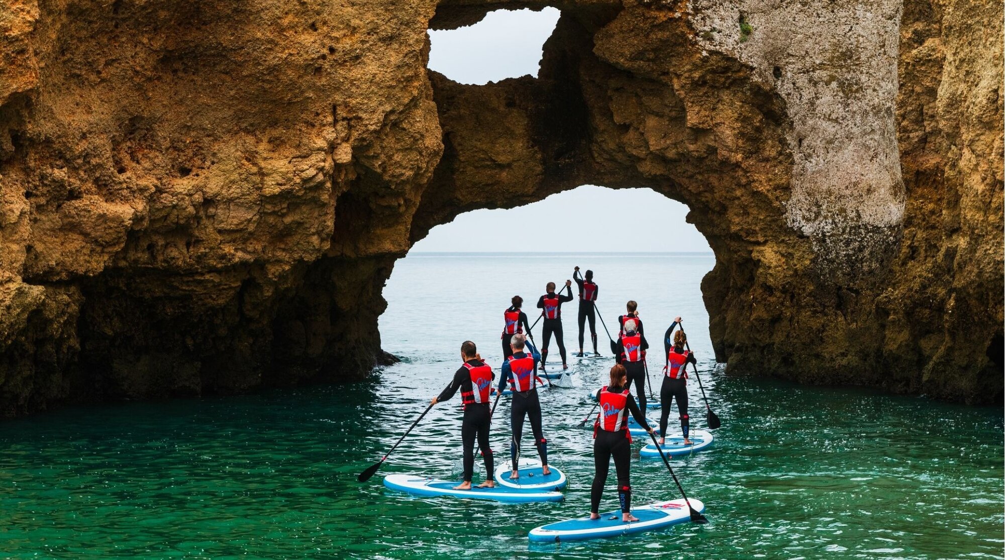 Grupo de praticantes de stand-up paddle explorando a Ponta da Piedade no Algarve, Portugal, com impressionantes formações rochosas.