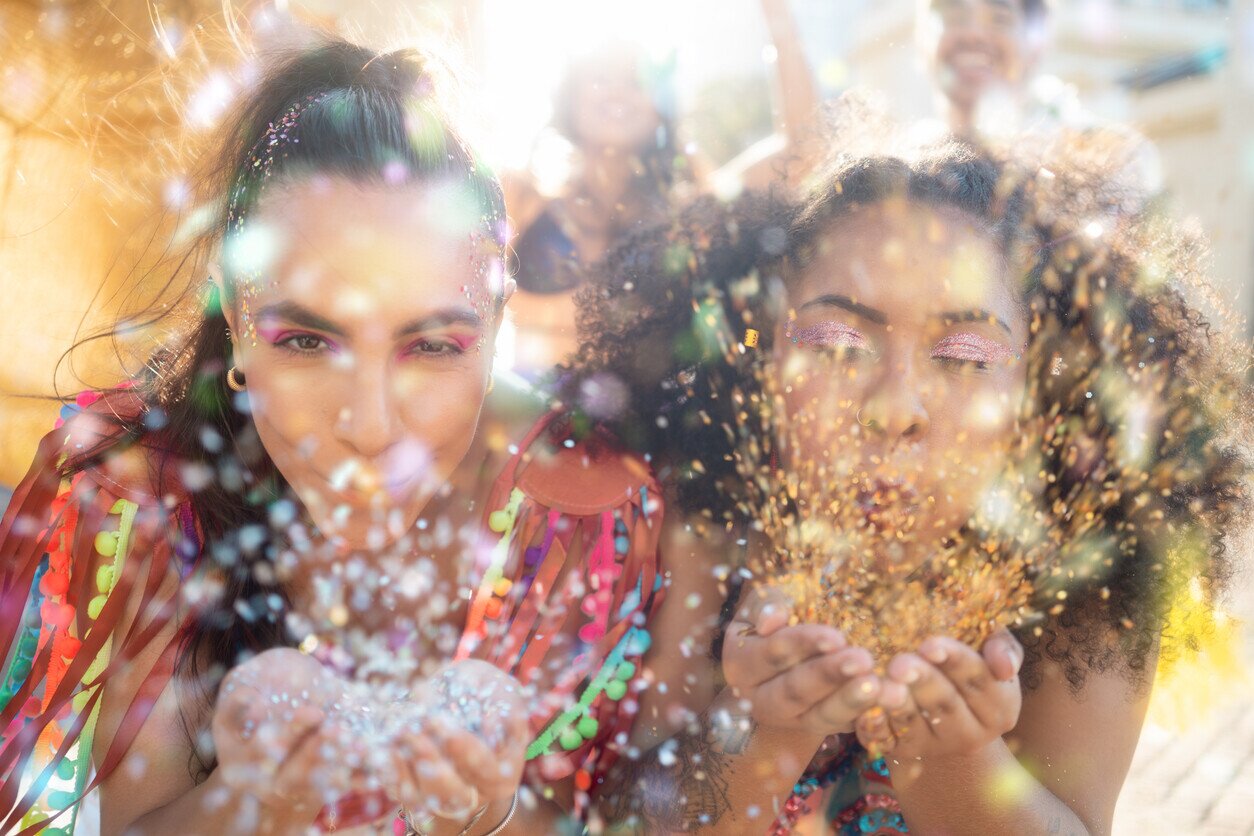 Zwei Frauen pusten bunten Glitter in die Kamera auf dem Karneval in Rio.
