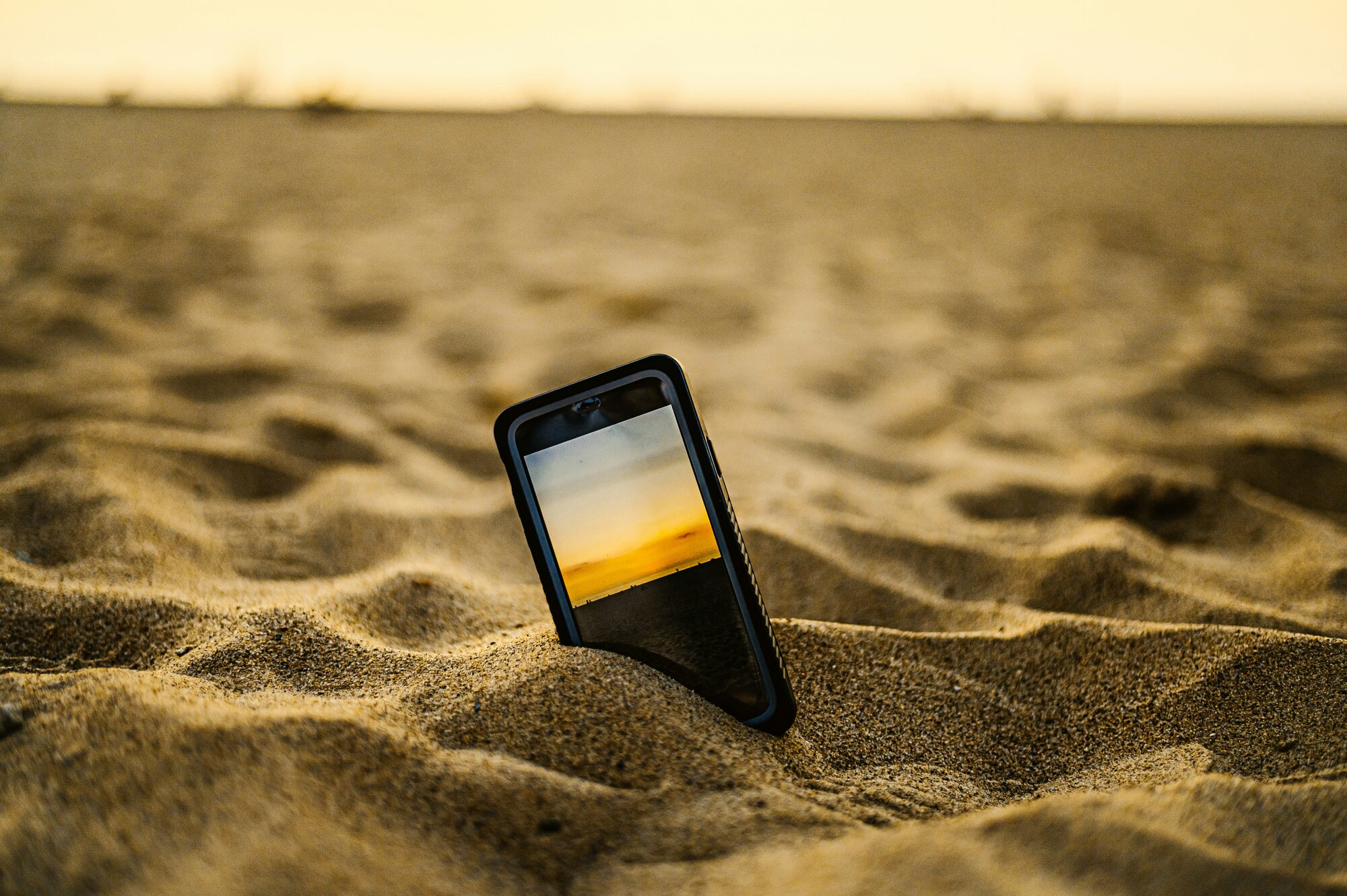 Celular parcialmente enterrado en la arena de la playa para ilustrar la conexión a internet.