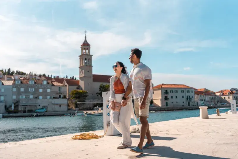 Pareja caminando junto al mar en un paseo costero en Sutivan con edificios al fondo.