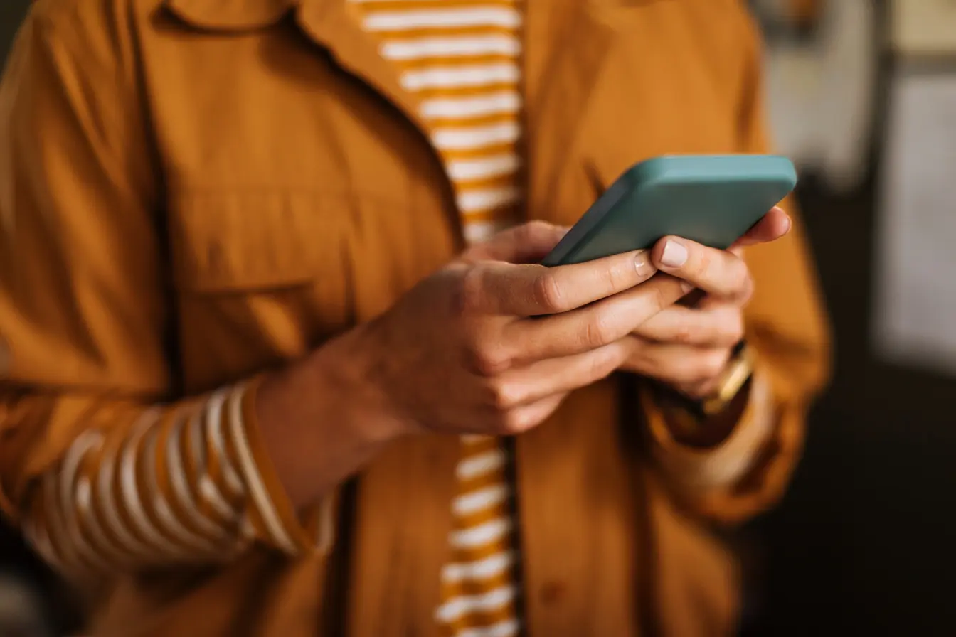 Gros plan sur les mains d'un utilisateur manipulant son smartphone à la recherche du meilleur forfait international.