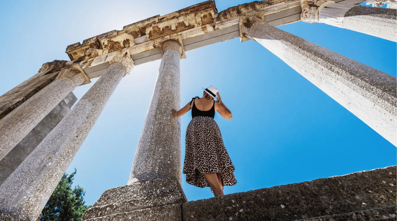 Femme debout devant un monument historique en Albanie sous un ciel bleu.