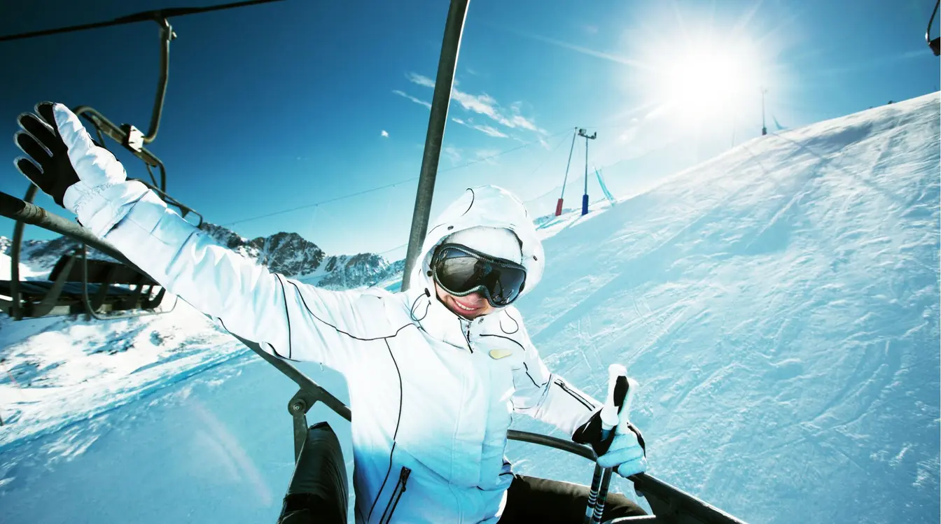 Esquiador en telesilla con gafas de nieve y chaqueta blanca, en una estación de esquí de montaña.