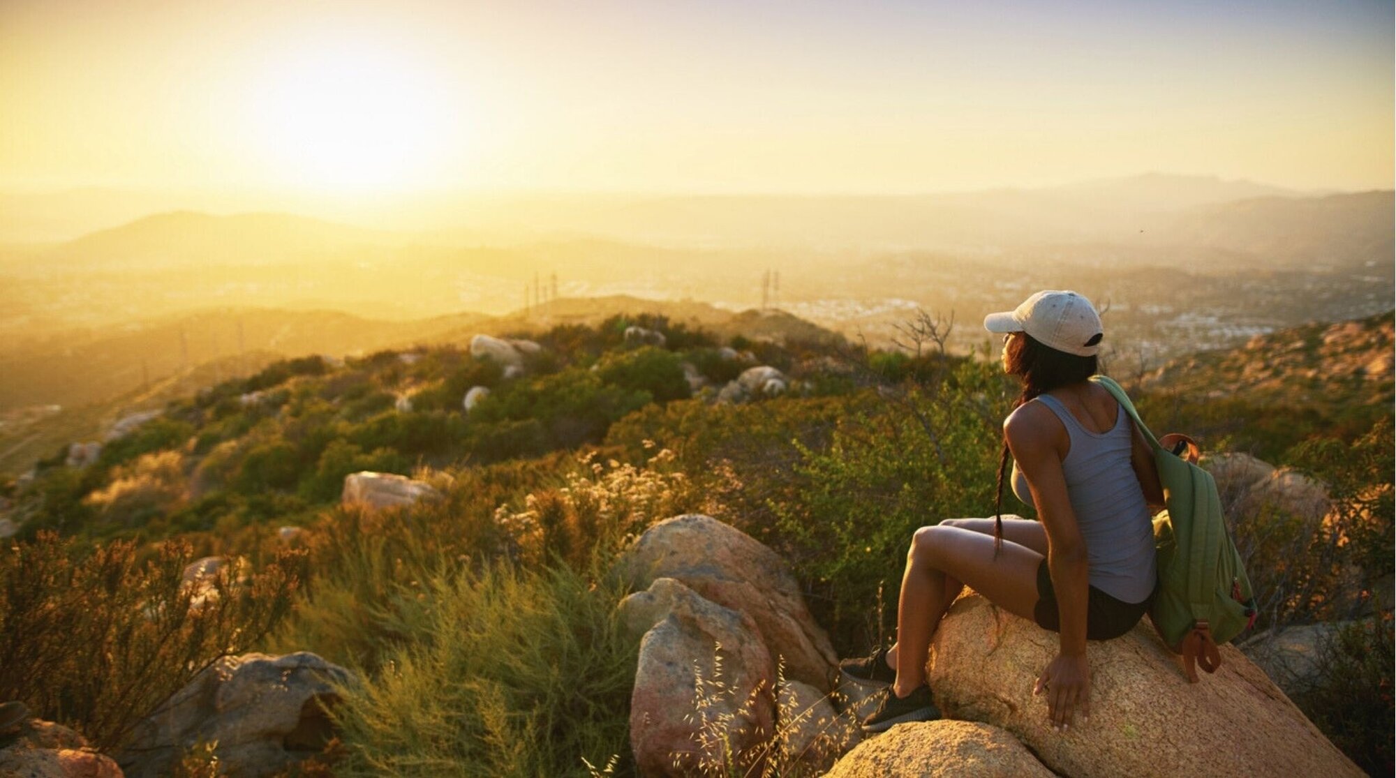 Viajera sentada en un mirador viendo el atardecer sobre las colinas de California.