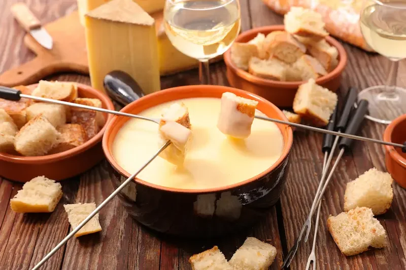 Fondue au fromage suisse servie dans un caquelon avec morceaux de pain et verres de vin blanc