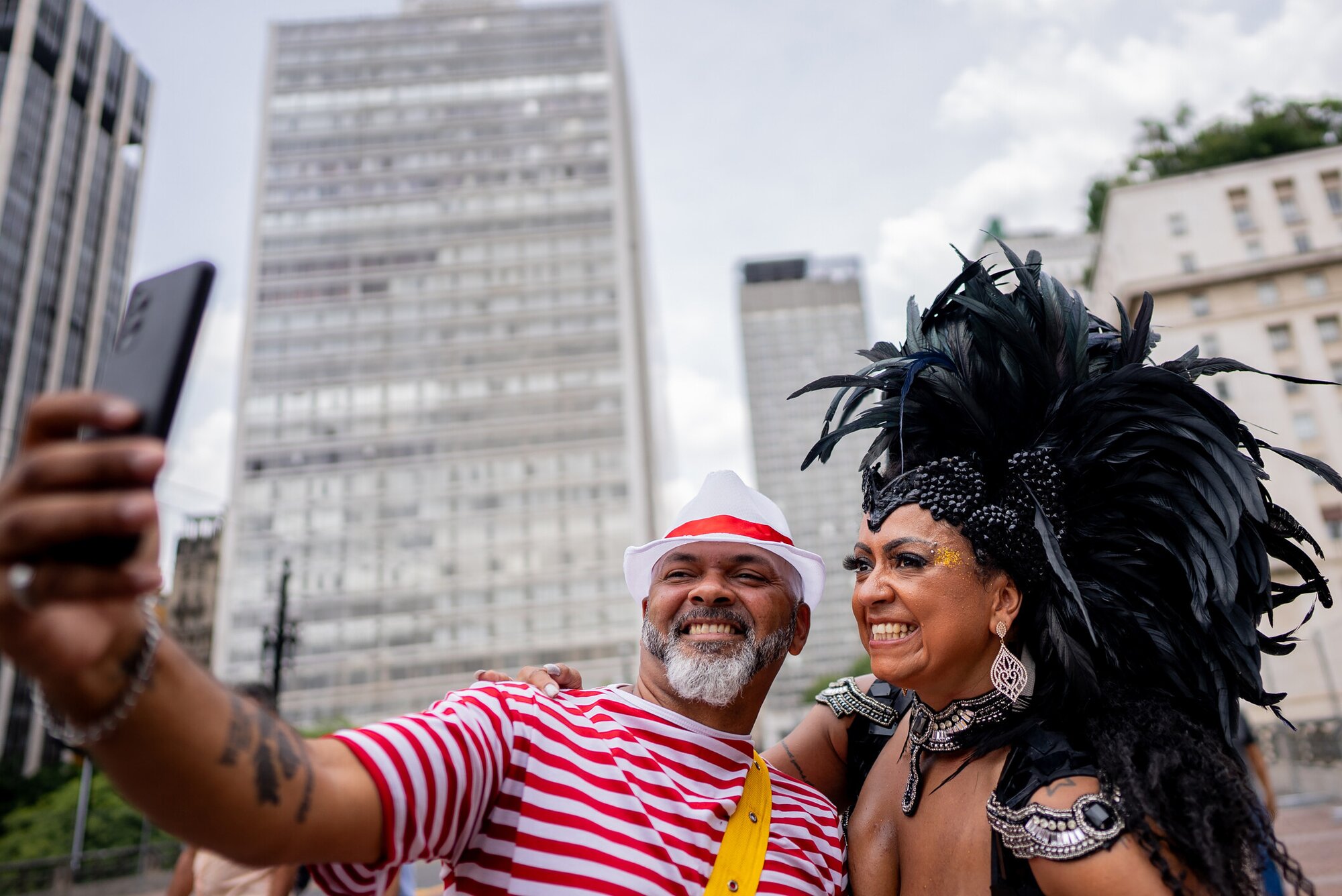Ein Mann mit einem Handy in der Hand steht neben einer verkleideten Frau beim Karneval in Rio