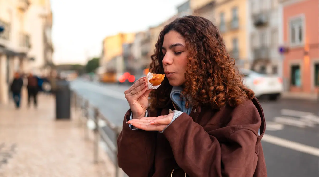Jovem viajante experimentando um dos principais quitutes de Portugal, o famoso pastel de Belém.