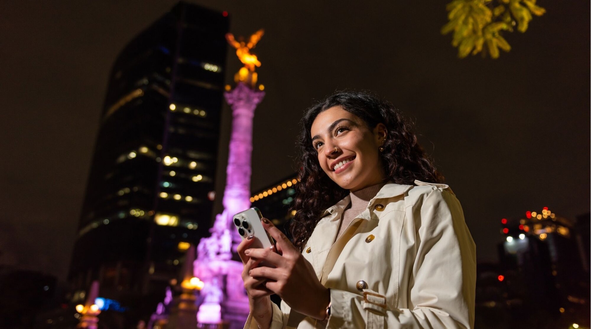 Viajante conectada utilizando seu smartphone em frente ao icônico monumento El Ángel de la Independencia, na Cidade do México.