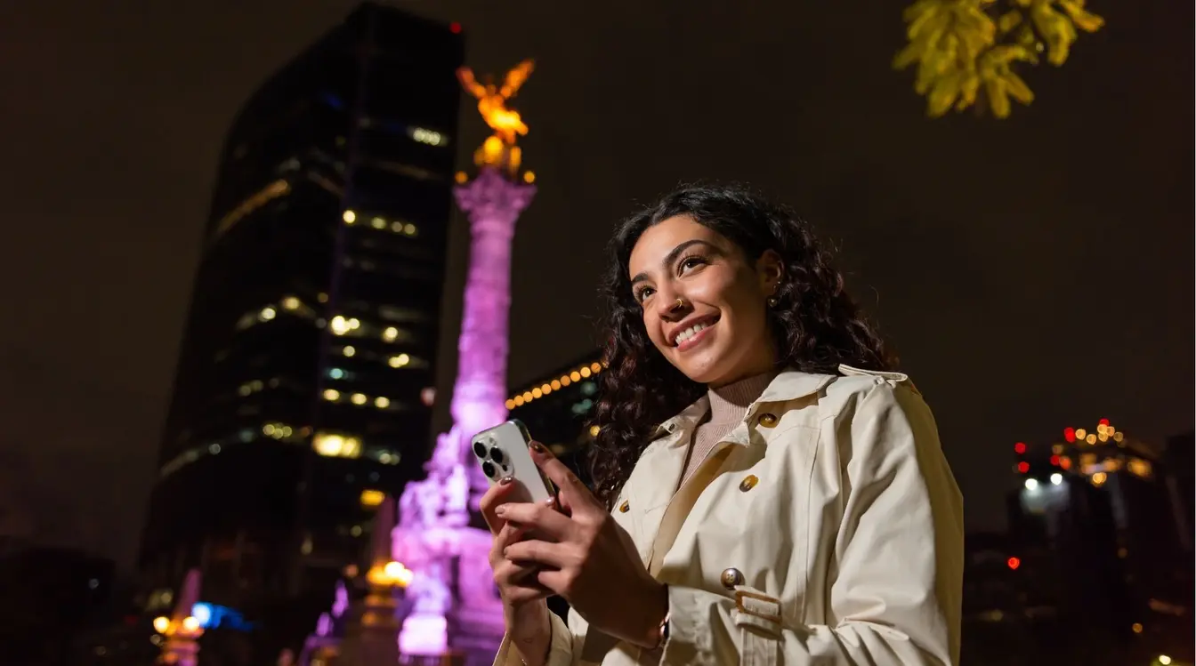 Viajante conectada utilizando seu smartphone em frente ao icônico monumento El Ángel de la Independencia, na Cidade do México.