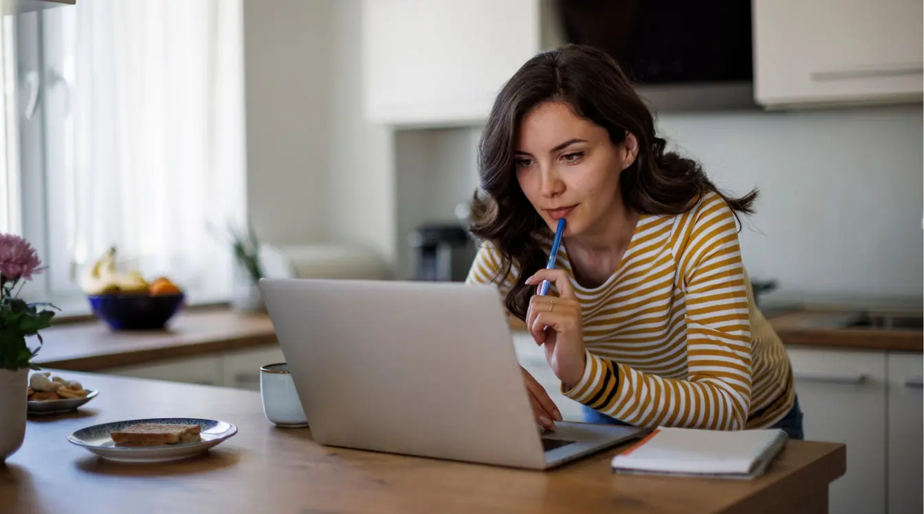 Jeune femme utilisant son ordinateur pour préparer son voyage depuis chez elle.