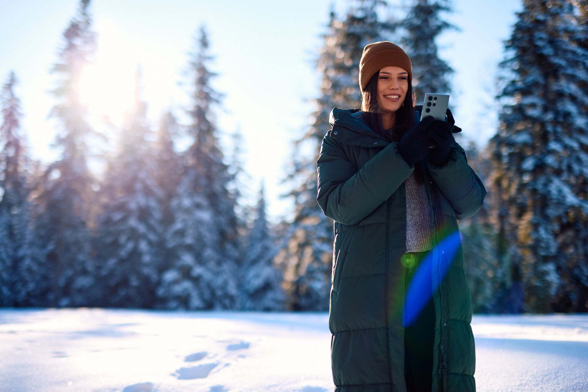 Junge Frau, die am sonnigen Wintertag Fotos mit einer eSIM im verschneiten Wald in Bosnien und Herzegowinamacht