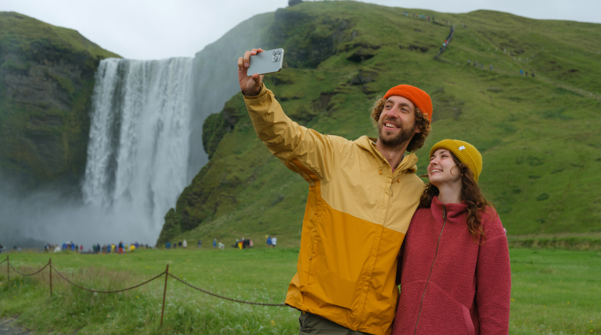 Uomo e donna scattano foto con lo smartphone davanti alla cascata Skógafoss in Islanda durante il viaggio
