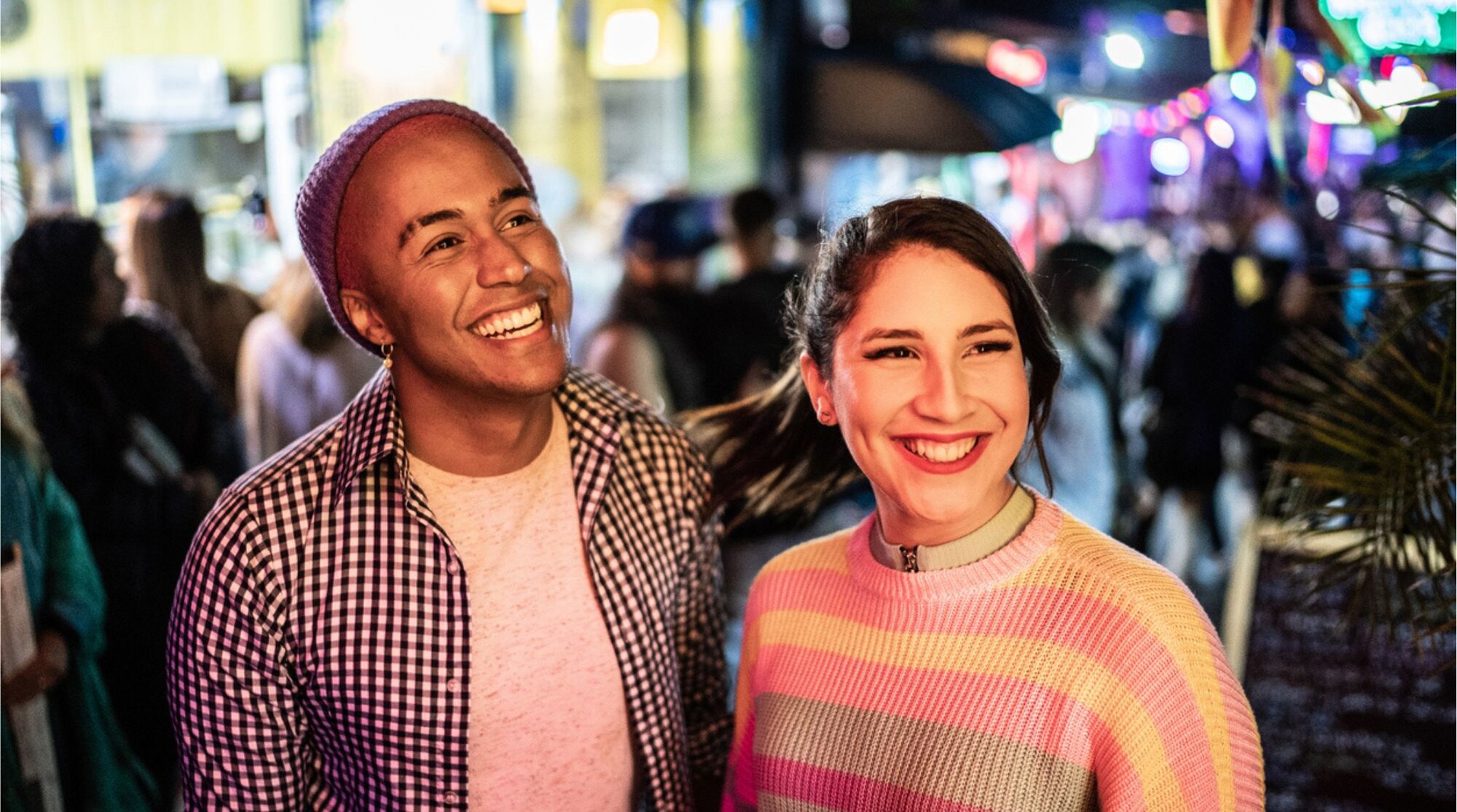 Pareja caminando de noche por una zona concurrida de Las Vegas, con luces de neón, gente y ambiente animado al fondo.
