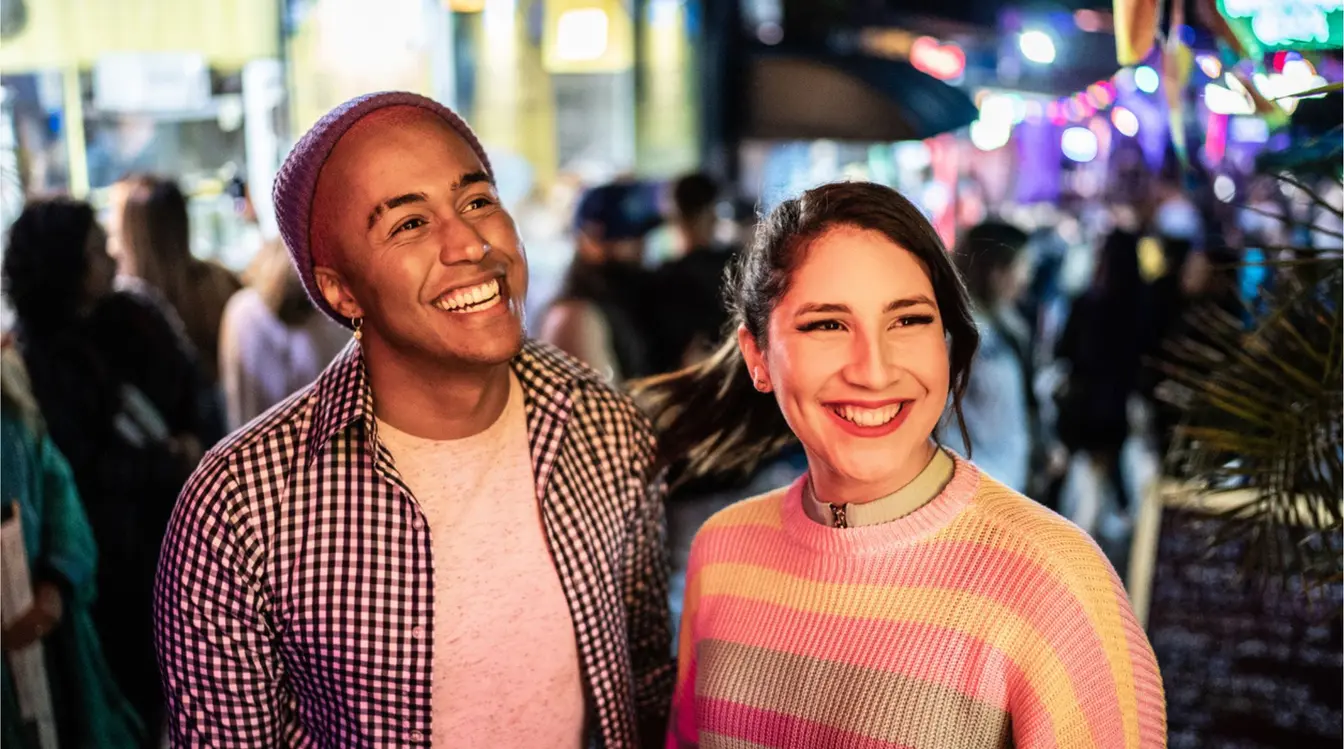 Pareja caminando de noche por una zona concurrida de Las Vegas, con luces de neón, gente y ambiente animado al fondo.